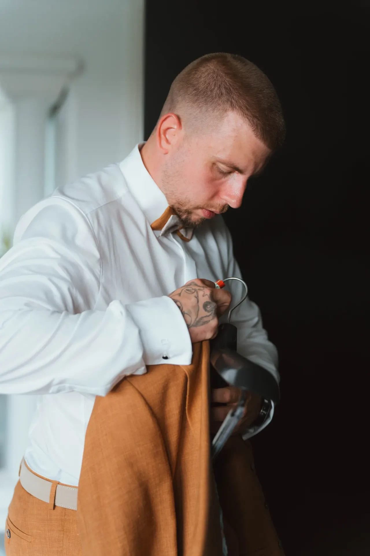 Bräutigam mit Tattoos richtet konzentriert seine cognacfarbene Krawatte